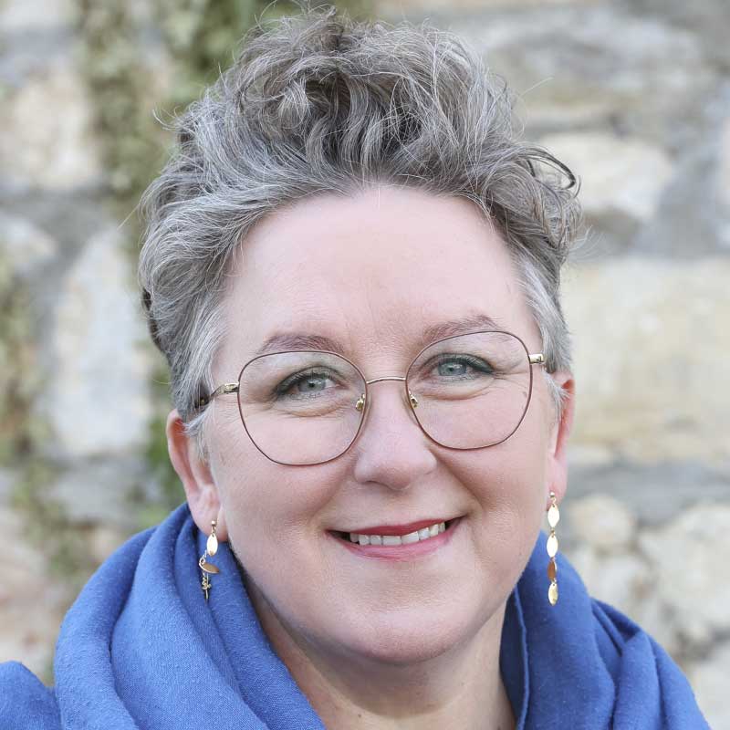 Eine Frau mit grauen Haaren und blauen Schal lächelt.