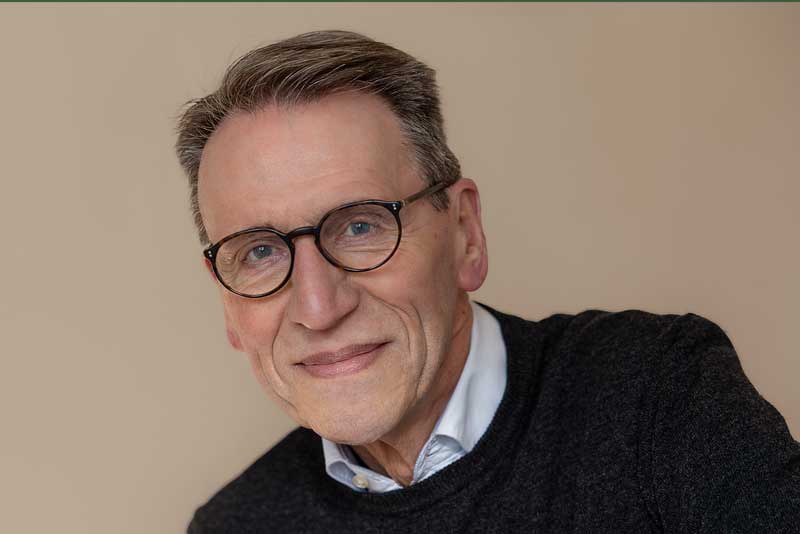 Ein älterer Mann mit Brille lächelt freundlich.