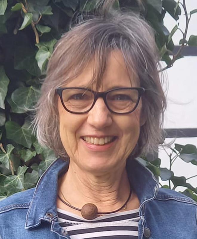 Eine Frau mit grauen Haaren und Brille lächelt