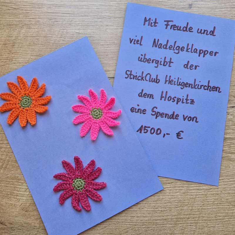 Eine blaue Karte mit drei handgemachten Blumen und ein Brief mit einer Spende von 500 Euro